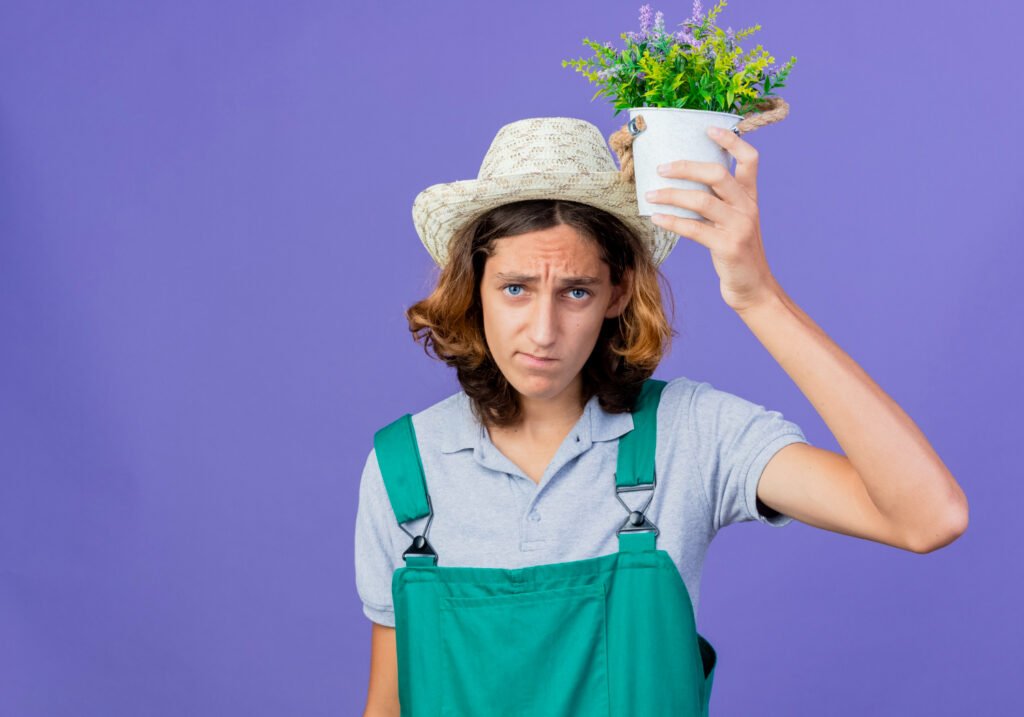 persona sosteniendo una maceta cerca de su cabeza, pensando por que falla en los cuidados de sus plantas de interior.